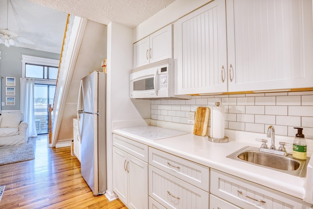 kitchen with light wood-type flooring, light countertops, white appliances, a textured ceiling, and a sink