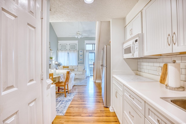 kitchen featuring white microwave, light wood-style flooring, freestanding refrigerator, ceiling fan, and light countertops