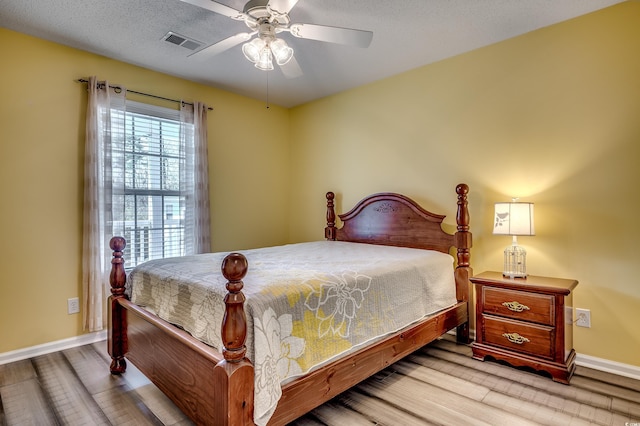 bedroom with wood finished floors, visible vents, baseboards, ceiling fan, and a textured ceiling