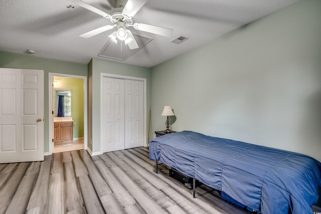 bedroom with wood finished floors, visible vents, baseboards, a closet, and a textured ceiling