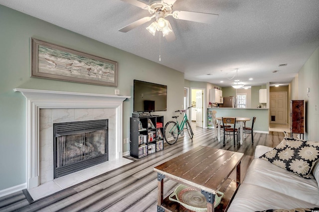 living room featuring a tiled fireplace, a ceiling fan, light wood finished floors, and a textured ceiling