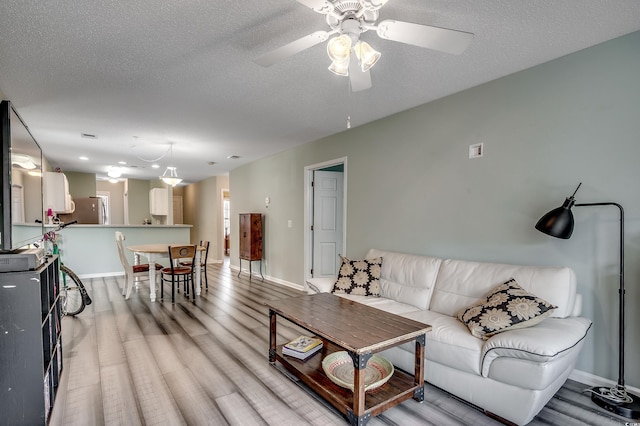 living room featuring ceiling fan, light wood-type flooring, and a textured ceiling