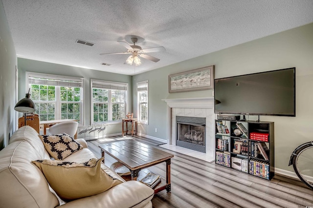 living area featuring a fireplace, wood finished floors, visible vents, and ceiling fan