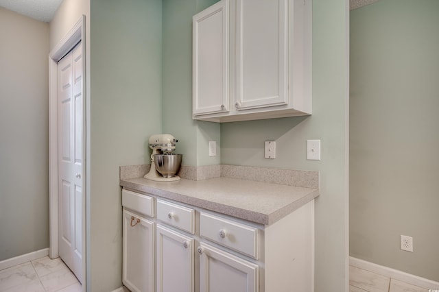 kitchen with marble finish floor, white cabinetry, light countertops, and baseboards