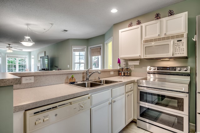 kitchen featuring visible vents, a sink, white appliances, a peninsula, and a healthy amount of sunlight