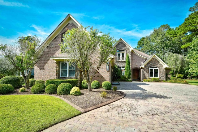 view of front of property featuring stone siding, driveway, a front lawn, and a balcony