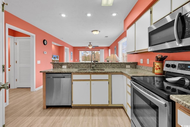 kitchen featuring a sink, stainless steel appliances, a peninsula, white cabinets, and light wood finished floors