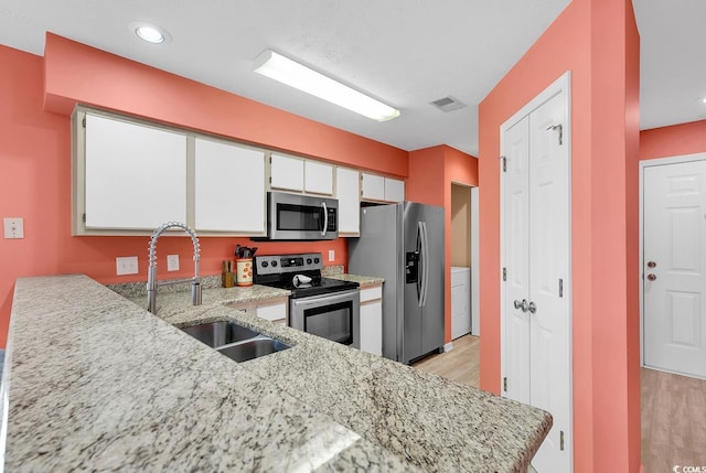 kitchen featuring light stone counters, visible vents, a sink, stainless steel appliances, and light wood-type flooring