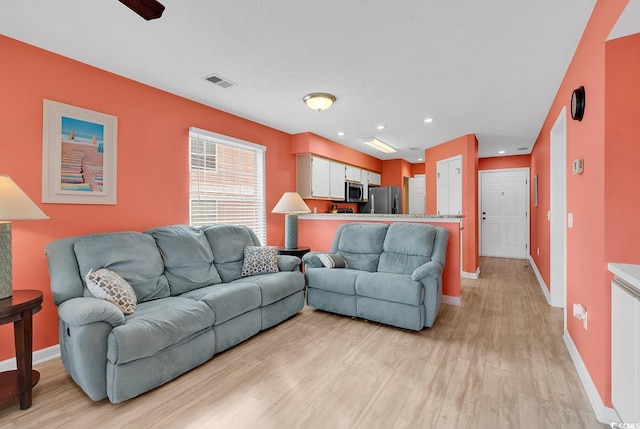 living room featuring visible vents, baseboards, and light wood finished floors