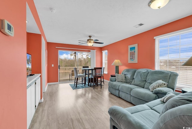 living room featuring light wood finished floors, visible vents, a healthy amount of sunlight, and a ceiling fan