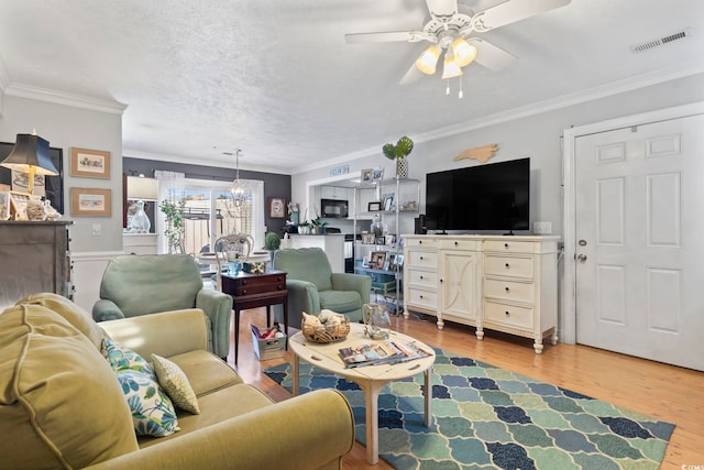 living room featuring ceiling fan with notable chandelier, crown molding, light wood-style floors, and visible vents