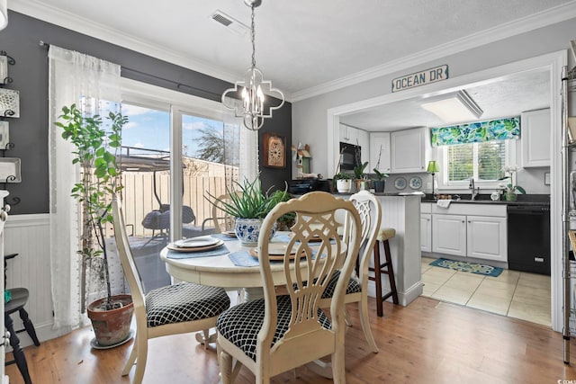 dining area with visible vents, a wainscoted wall, ornamental molding, light wood-type flooring, and a chandelier