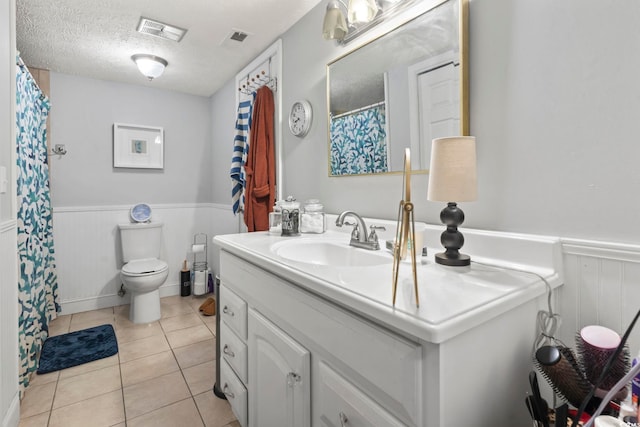 bathroom featuring a wainscoted wall, toilet, visible vents, and a textured ceiling