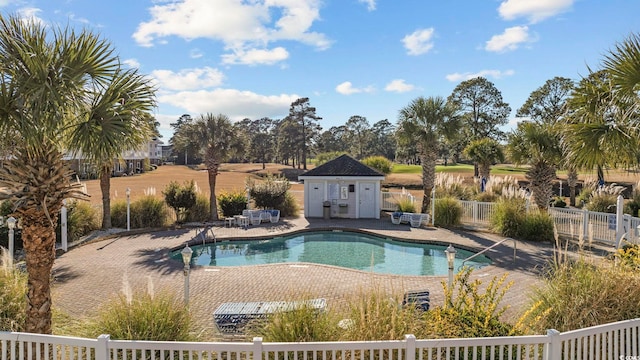 community pool with a patio area, an outdoor structure, and fence