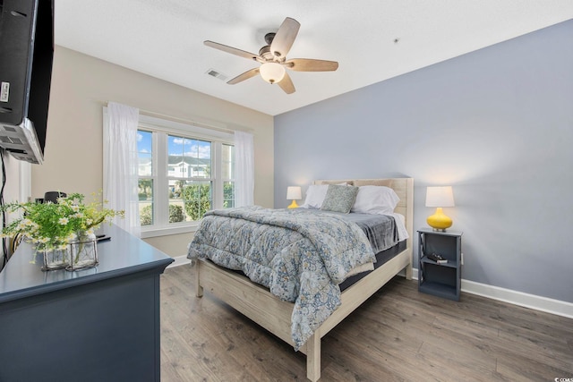 bedroom with ceiling fan, wood finished floors, visible vents, and baseboards