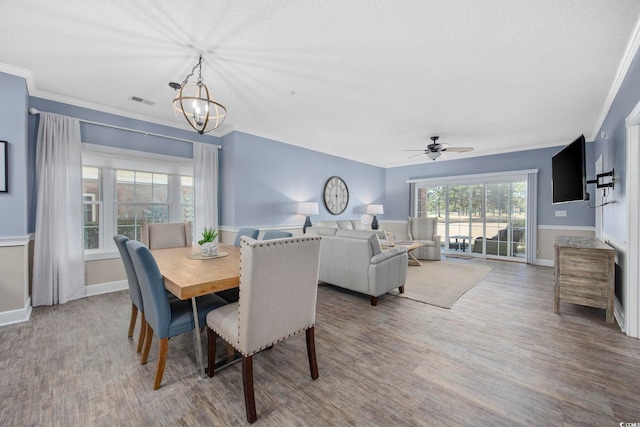 dining space with visible vents, ornamental molding, ceiling fan with notable chandelier, wood finished floors, and baseboards