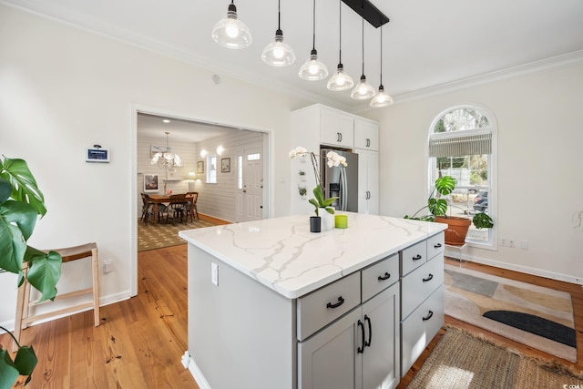 kitchen with ornamental molding, a center island, light wood-style floors, stainless steel fridge with ice dispenser, and light stone countertops