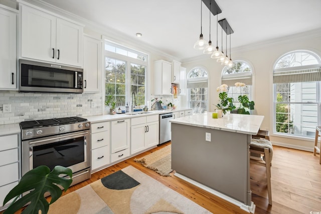 kitchen with a breakfast bar, a sink, a center island, appliances with stainless steel finishes, and crown molding