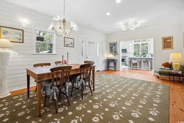 dining space featuring a healthy amount of sunlight, ornamental molding, an inviting chandelier, and wood finished floors