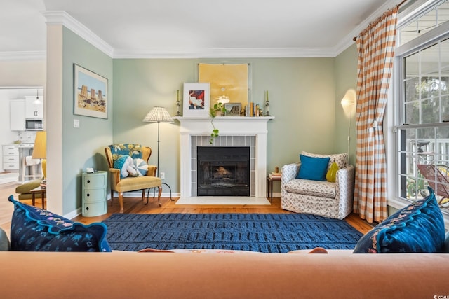 living area with baseboards, wood finished floors, crown molding, and a tiled fireplace