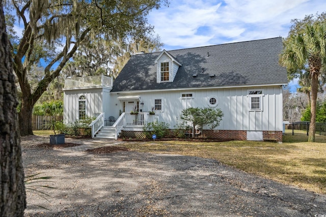 view of front facade with board and batten siding, a shingled roof, a balcony, and fence