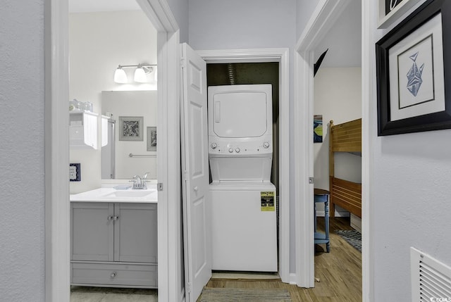 laundry area with wood finished floors, visible vents, laundry area, a sink, and stacked washer / drying machine