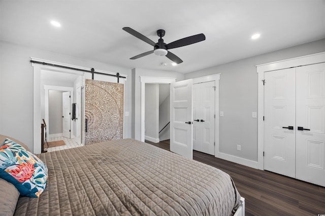 bedroom with two closets, dark wood-style floors, recessed lighting, a barn door, and baseboards