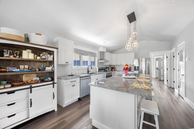 kitchen featuring light stone counters, lofted ceiling, stainless steel appliances, white cabinets, and wall chimney exhaust hood