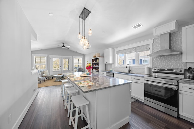 kitchen with visible vents, a sink, vaulted ceiling, appliances with stainless steel finishes, and wall chimney exhaust hood