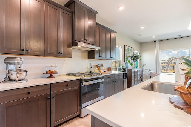 kitchen with under cabinet range hood, light countertops, stainless steel gas range, and a sink