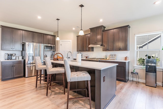 kitchen with stainless steel appliances, dark brown cabinetry, a breakfast bar, and light countertops