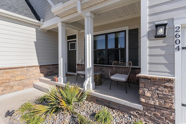 entrance to property featuring covered porch and a shingled roof