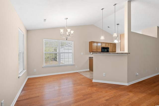 kitchen with black microwave, a chandelier, vaulted ceiling, brown cabinets, and light wood-style floors