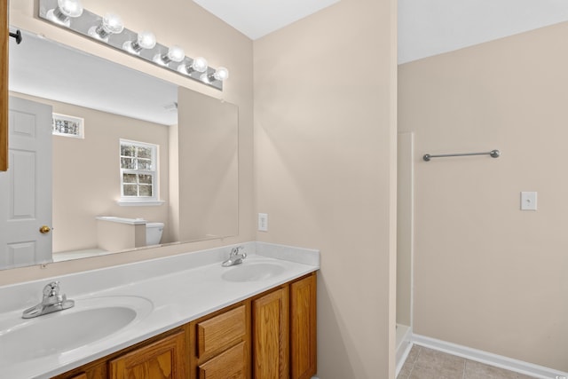 bathroom with double vanity, toilet, baseboards, and a sink