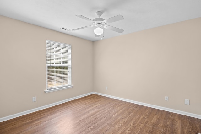 empty room featuring ceiling fan, visible vents, baseboards, and wood finished floors