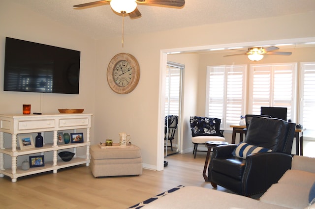 living room with baseboards, light wood-style flooring, a textured ceiling, and a ceiling fan