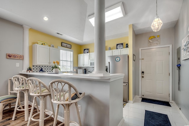 kitchen with ornate columns, a peninsula, freestanding refrigerator, decorative backsplash, and a kitchen breakfast bar