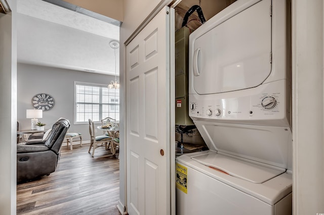 clothes washing area featuring laundry area, wood finished floors, stacked washer and clothes dryer, and baseboards