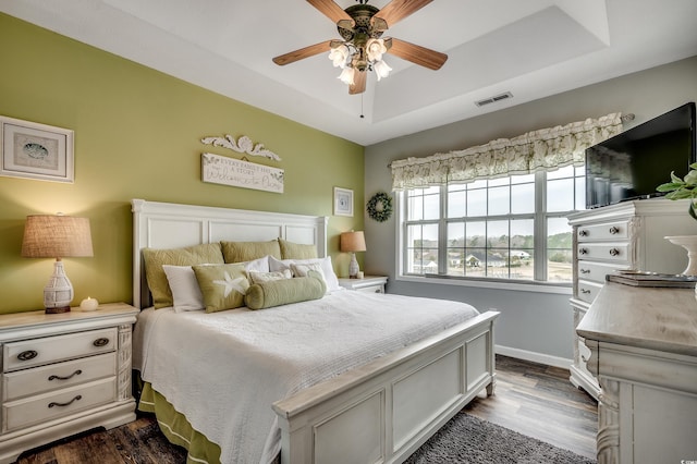 bedroom featuring visible vents, a raised ceiling, baseboards, and dark wood-style flooring