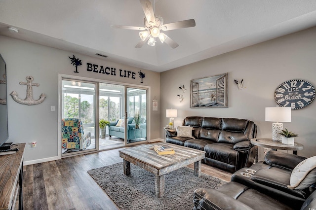 living area with visible vents, baseboards, a tray ceiling, wood finished floors, and a ceiling fan