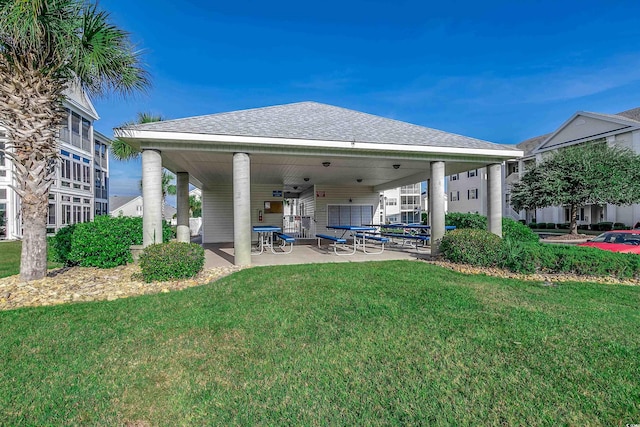 rear view of house featuring a yard, a patio, and roof with shingles