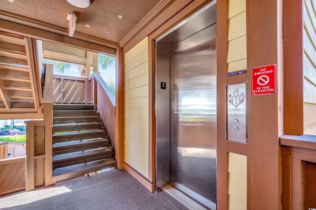 stairway with crown molding, elevator, and carpet