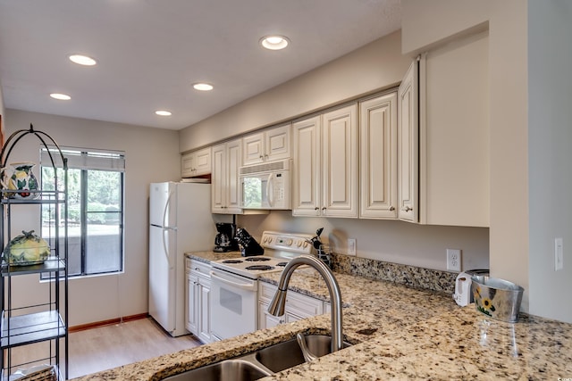 kitchen featuring light wood-style flooring, light stone counters, a sink, recessed lighting, and white appliances