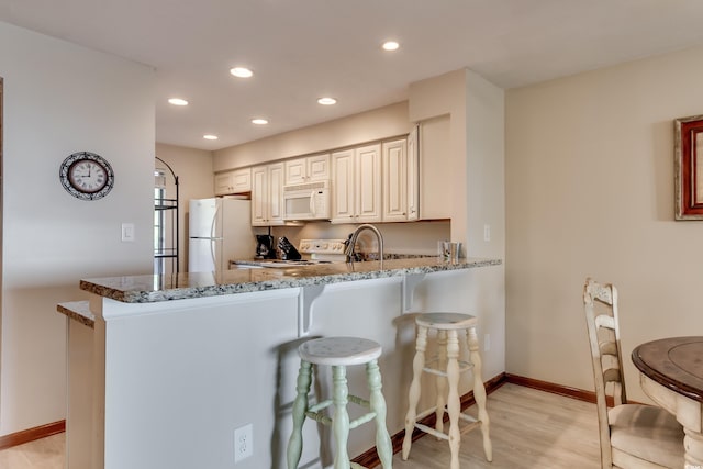 kitchen with a kitchen bar, stone countertops, recessed lighting, white appliances, and a peninsula