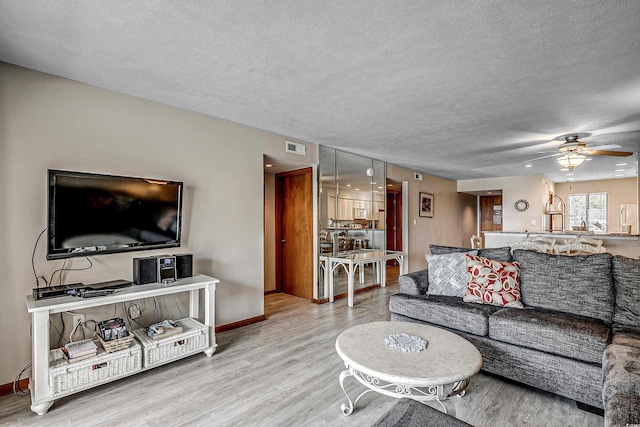 living area featuring visible vents, baseboards, wood finished floors, a textured ceiling, and a ceiling fan