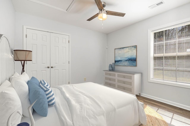 bedroom with wood finished floors, visible vents, baseboards, ceiling fan, and a closet