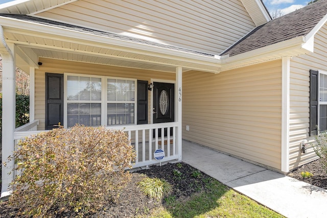 view of exterior entry featuring roof with shingles and a porch