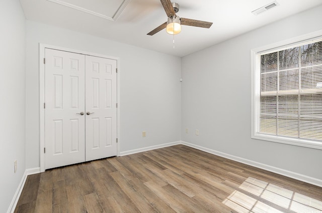 unfurnished bedroom with wood finished floors, visible vents, baseboards, ceiling fan, and a closet