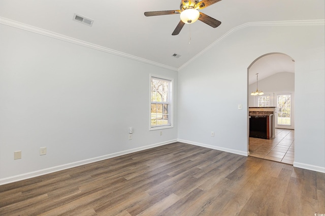 empty room featuring visible vents, dark wood finished floors, lofted ceiling, arched walkways, and ornamental molding