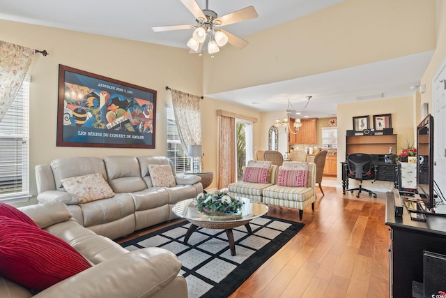 living room with visible vents, ceiling fan with notable chandelier, vaulted ceiling, and light wood finished floors